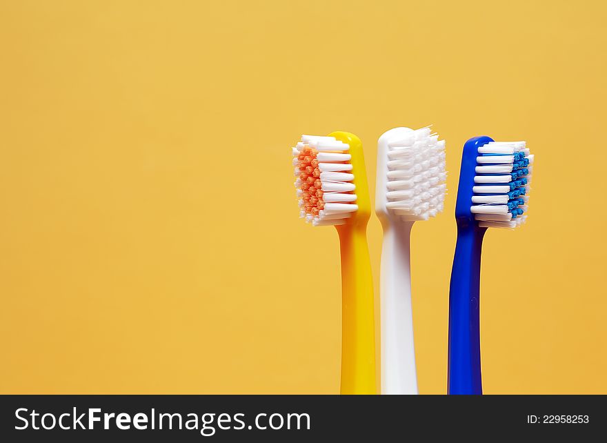 Three multicolored toothbrushes on yellow background with free space for text