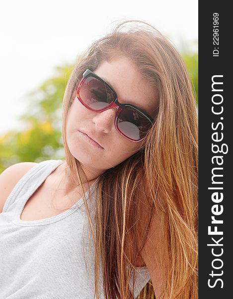 Teen girl outdoors wearing sunglasses, a gray tank top, and long hair. Teen girl outdoors wearing sunglasses, a gray tank top, and long hair