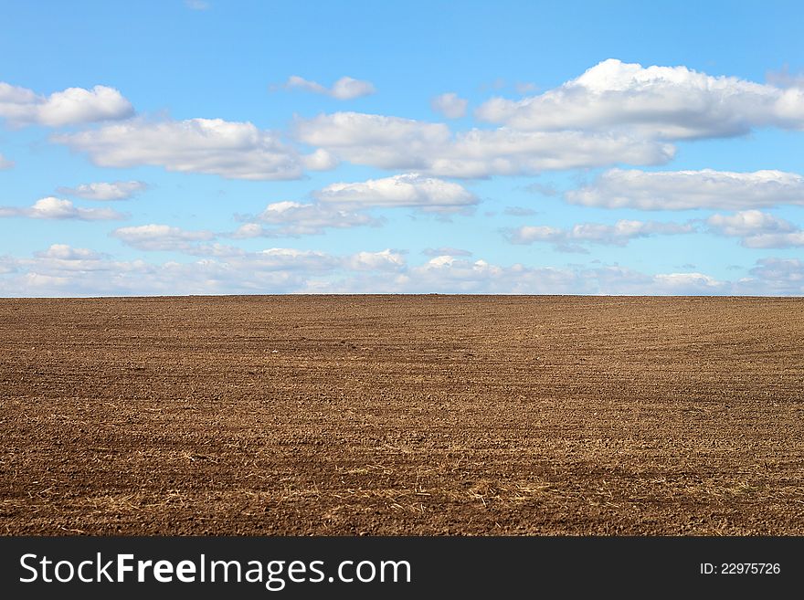 Ploughed field below the blue cloudy sky. Ploughed field below the blue cloudy sky
