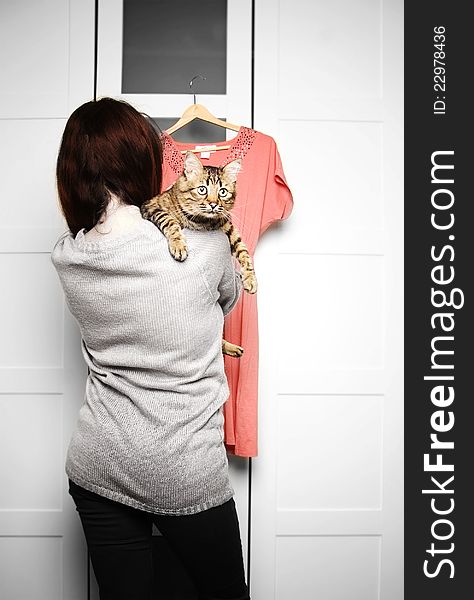 Young woman holding a cat is looking at a dress in front of wardrobe