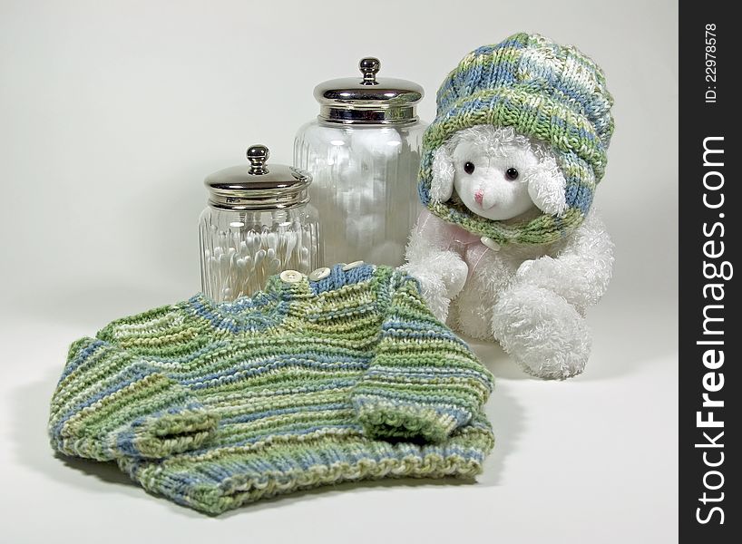 A baby’s hand-knit sweater and matching hat on a toy lamb along with cotton balls and Q-tips in apothecary jars. A baby’s hand-knit sweater and matching hat on a toy lamb along with cotton balls and Q-tips in apothecary jars