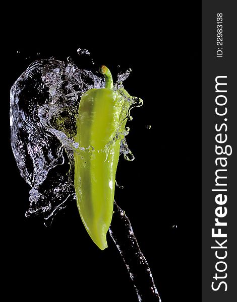 Green pepper splashed by water over black background