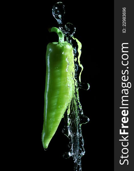 Green pepper splashed by water over black background