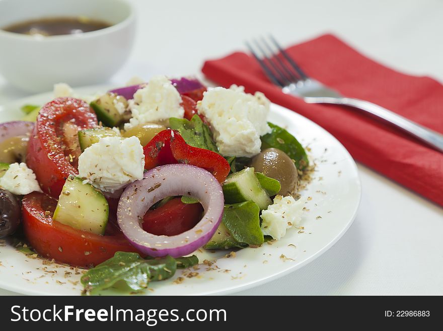 Traditional Greek salad with tomatoes, cucumber, lettuce, olives, peppers and feta cheese served on a white plate