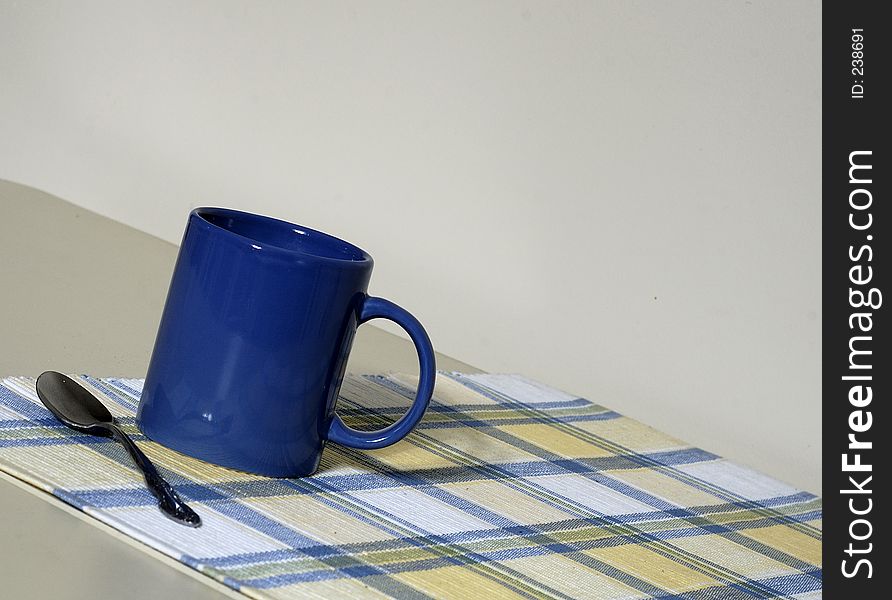 A close-up view of a coffee mug and spoon sitting on a placemat. A close-up view of a coffee mug and spoon sitting on a placemat