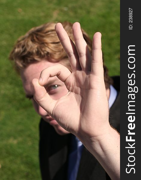 Through the OK sign, a businessman's eye can be seen, with green grass background. Through the OK sign, a businessman's eye can be seen, with green grass background