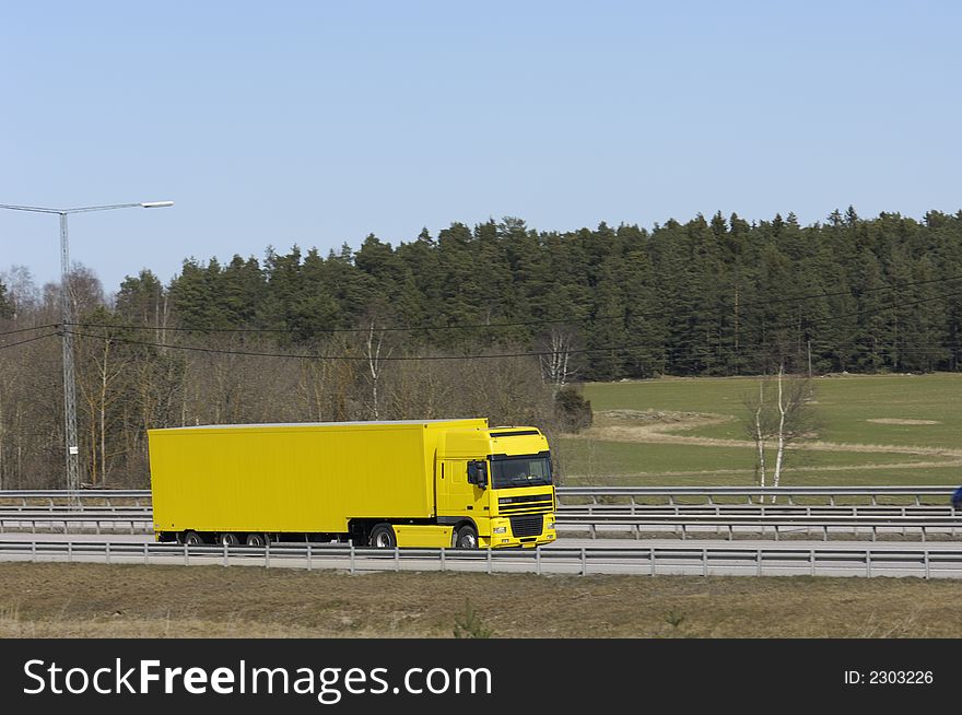 Clean yellow truck driving against spring-green foliage. Clean yellow truck driving against spring-green foliage