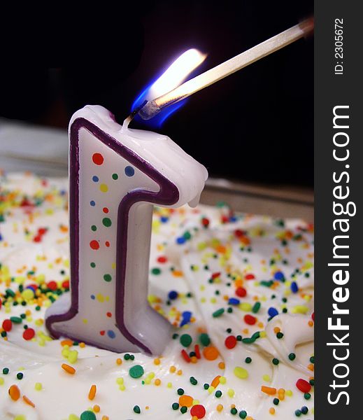 Number one birthday candle on cake with colorful sprinkles being lit with match. Number one birthday candle on cake with colorful sprinkles being lit with match
