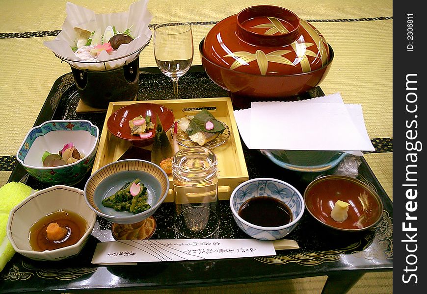 Tray with several different Japanese dishes in bowls, standing on a small low table on bamboo mats