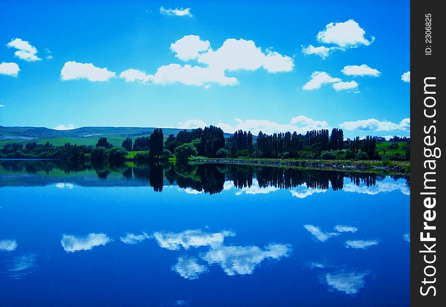 Beautiful blue sky with a few clouds and trees mirrored in calm lake surface. Beautiful blue sky with a few clouds and trees mirrored in calm lake surface