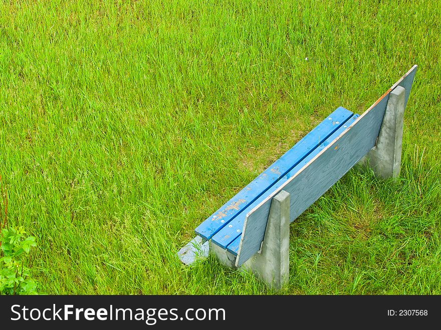Empty blue bench sitting in corner of field of green grass. Empty blue bench sitting in corner of field of green grass