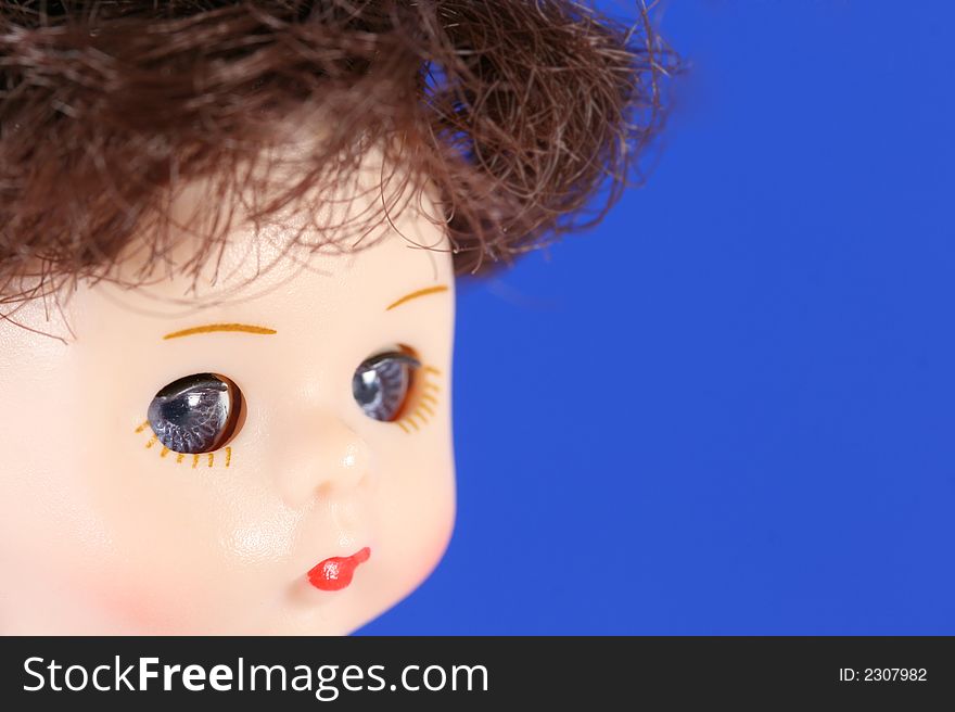 A close up of a doll's face with blue eyes and brown hair. A close up of a doll's face with blue eyes and brown hair