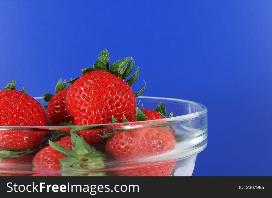 A bowl of organic strawberries with a vibrant blue background