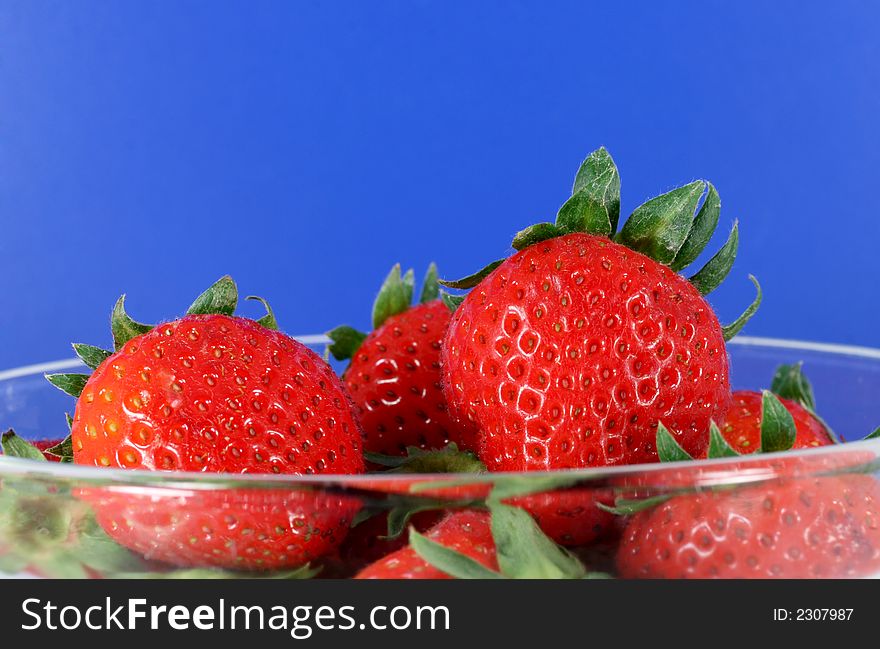 A glass bowl full of organic strawberries with a bright blu background. A glass bowl full of organic strawberries with a bright blu background