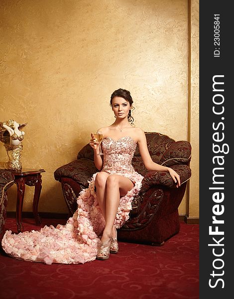 Beautiful bride in unusual wedding dress in the interior sitting in armchair with a cup of wine