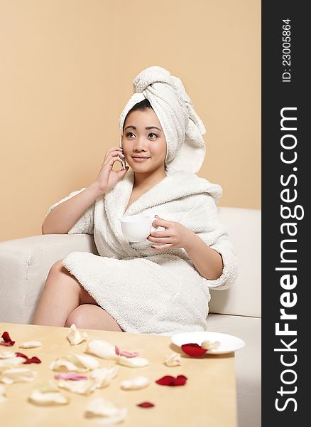 Portrait of pretty Chinese  businesswoman in white bathrobe with towel on head speaking on phone with cup of coffee. Portrait of pretty Chinese  businesswoman in white bathrobe with towel on head speaking on phone with cup of coffee