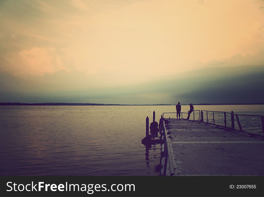 Fellow and girl stand on the pier of lake in the evening. Fellow and girl stand on the pier of lake in the evening