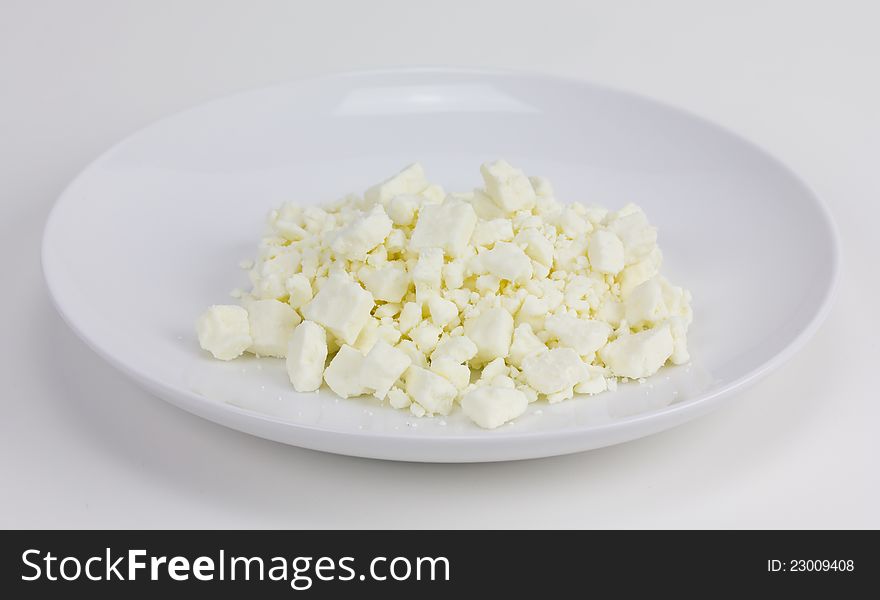 A small white plate of crumbled Feta cheese sitting on a white background.