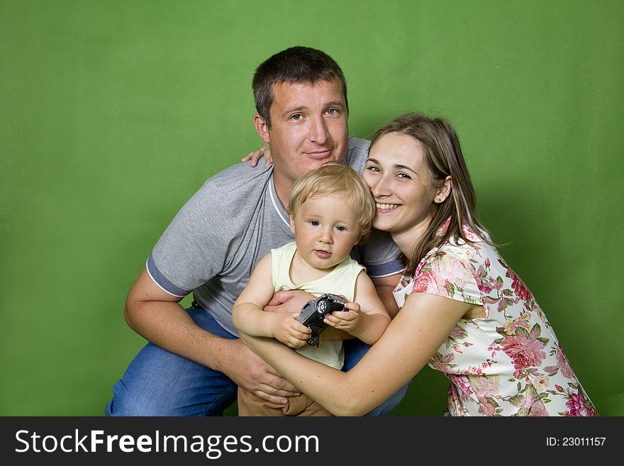 Young European family from three persons - mother, father and son. On a green background. Young European family from three persons - mother, father and son. On a green background.