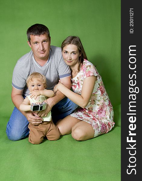 Young European family from three persons - mother, father and son. On a green background. Young European family from three persons - mother, father and son. On a green background.