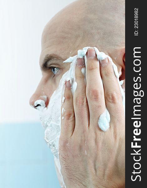 Young man applying shaving foam to face photographed in profile. Young man applying shaving foam to face photographed in profile