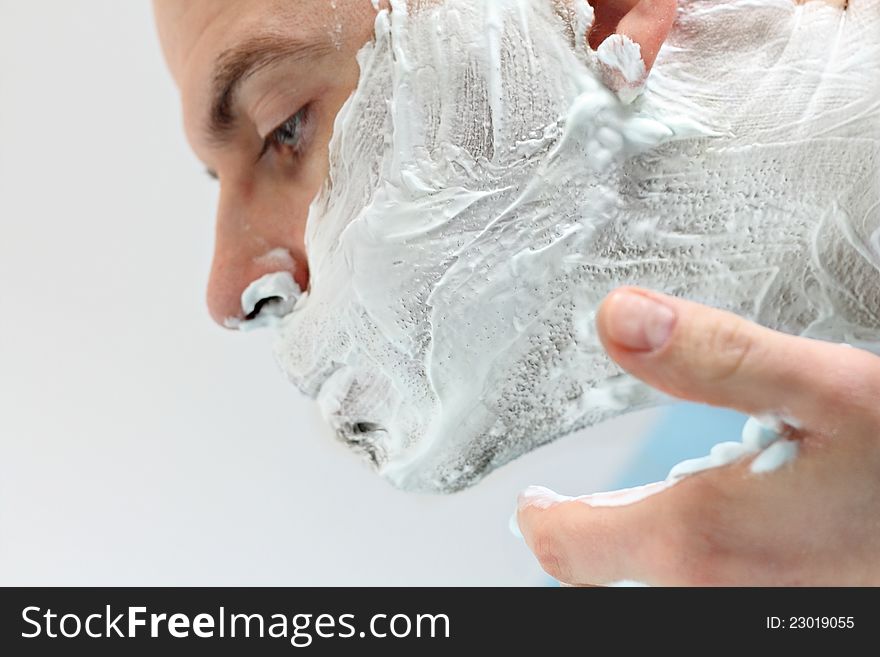 Young man applying shaving foam to face photographed in profile. Young man applying shaving foam to face photographed in profile