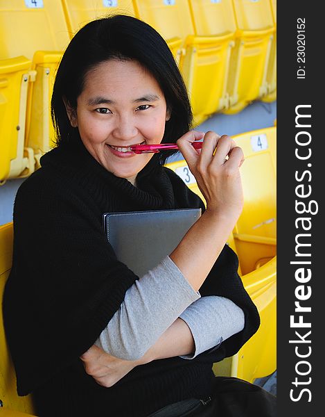 Young Asian college student hold book and pen sitting on grandstand to present education concept. Young Asian college student hold book and pen sitting on grandstand to present education concept