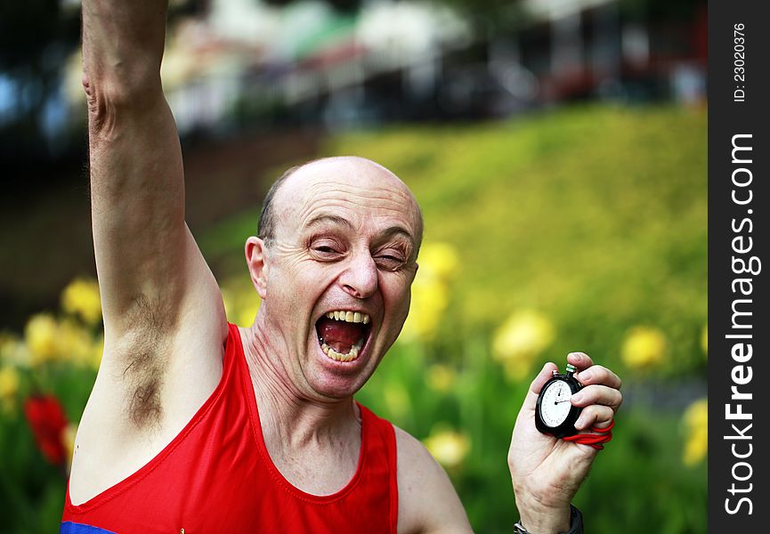 A close up of a businessman dressed in running attire, with a stopwatch in his hand elated that he has just broken his personal best time in a beautiful park. A close up of a businessman dressed in running attire, with a stopwatch in his hand elated that he has just broken his personal best time in a beautiful park.