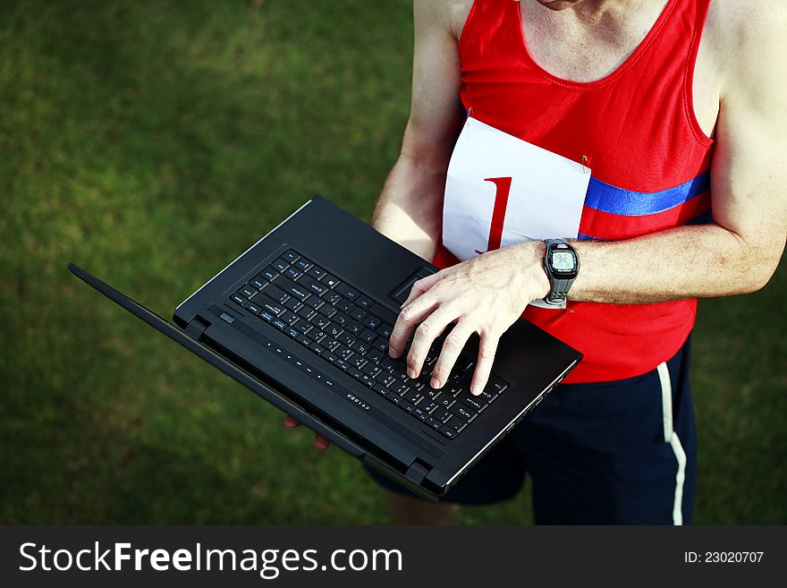 A close up of a businessman dressed in running attire with the number one on his chest, working on his laptop outside. A close up of a businessman dressed in running attire with the number one on his chest, working on his laptop outside.