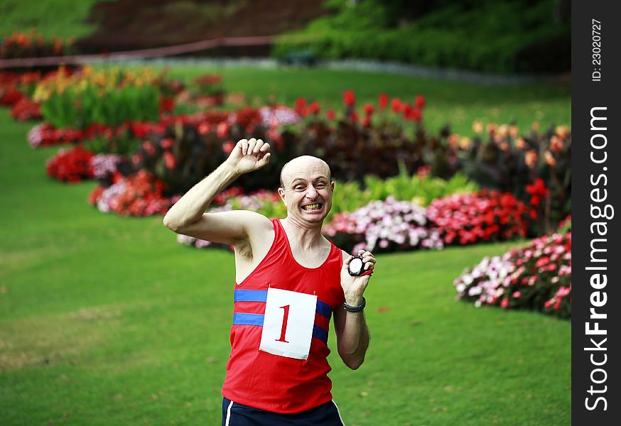 A close up of a man dressed in running attire, with a stopwatch in his hand elated that he has just broken his personal best time in a beautiful park. A close up of a man dressed in running attire, with a stopwatch in his hand elated that he has just broken his personal best time in a beautiful park.