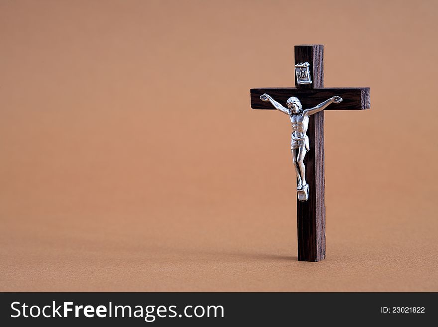 Faith concept.Small wooden crucifix standing on brown background with free space for text