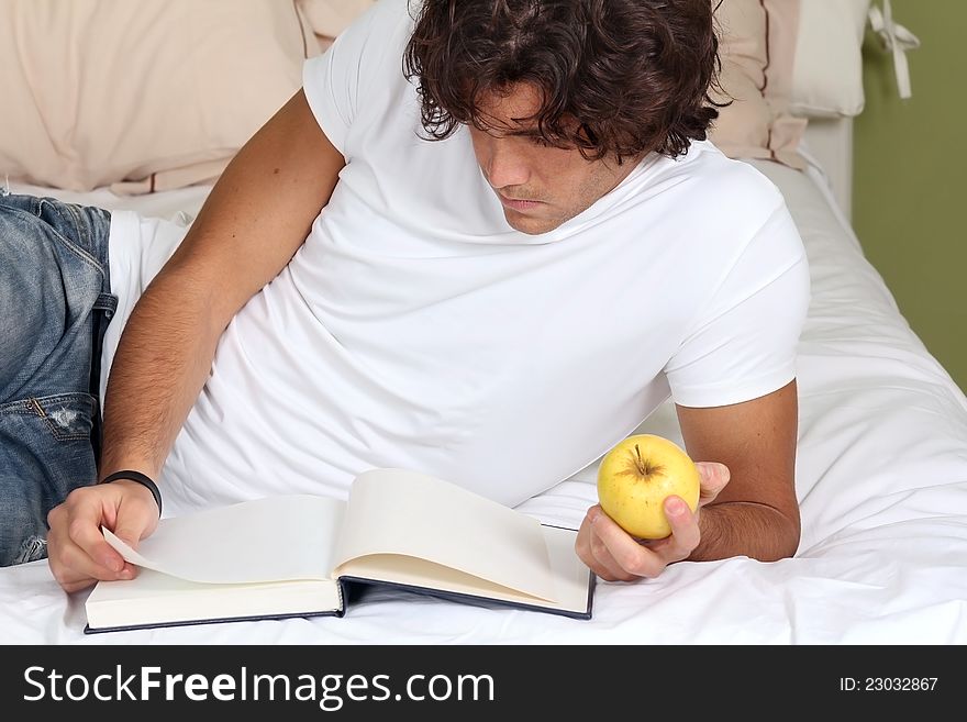 Young man focused on a book with an apple in hand. Young man focused on a book with an apple in hand