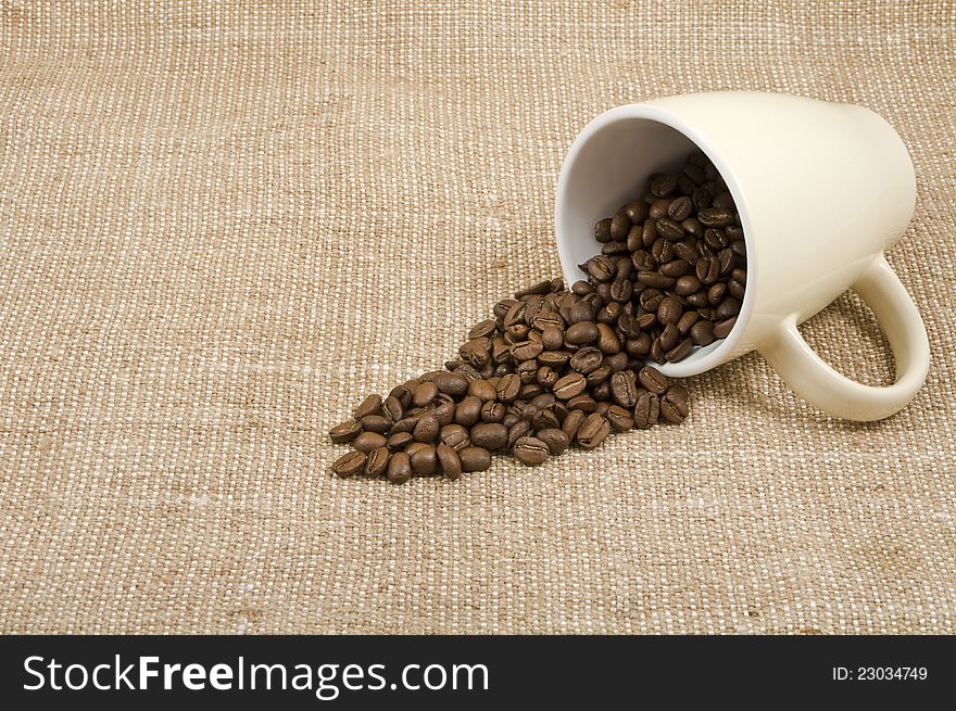 Grains of coffee pour out from a mug on a background sacking