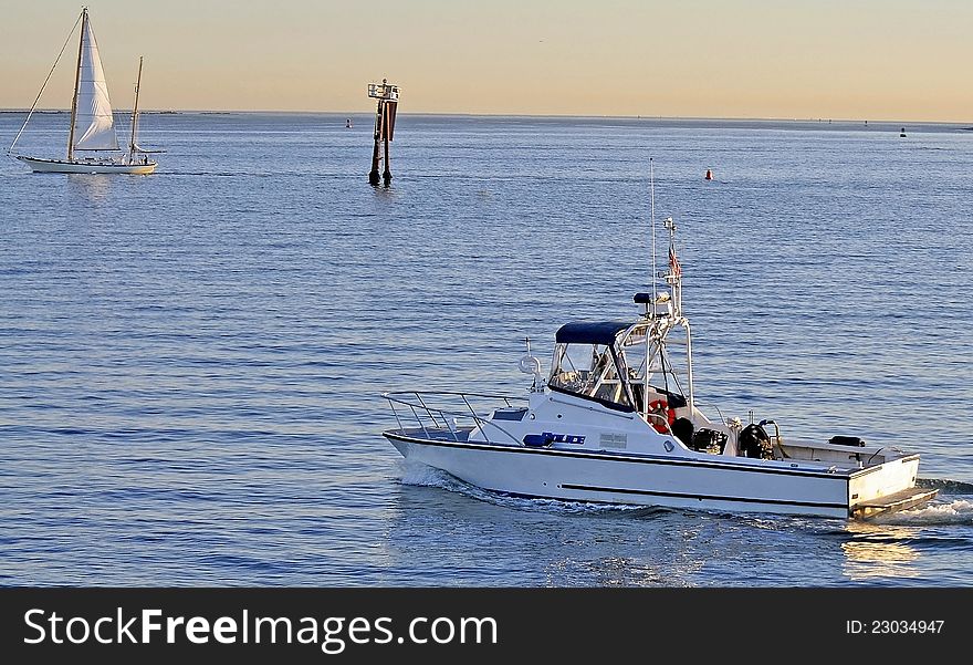 A Harbor Police Boat follows a Sailing Vessel into a Shipping Channel at Sunset. A Harbor Police Boat follows a Sailing Vessel into a Shipping Channel at Sunset.