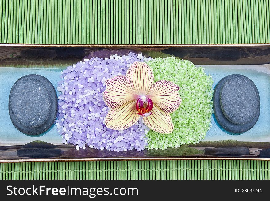 Spa concept with mineral bath salt, massage stones and orchid on green bamboo background