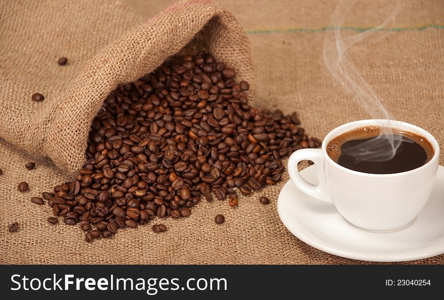 Cup with hot coffee and spilled coffee beans in addition to