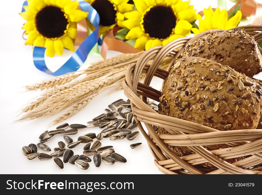 Whole-grain bread in a basked, sunflower seeds, wheat ears, sunflowers  and colored ribbons on a white background.
