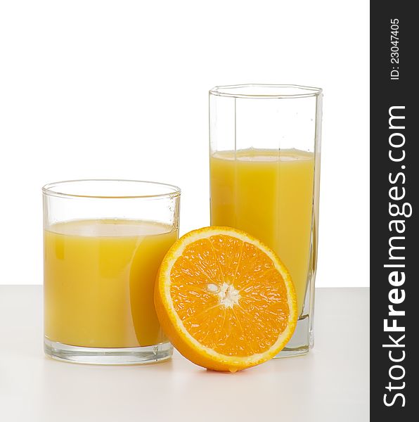 Two glasses of orange juice and sliced ripe orange on white background