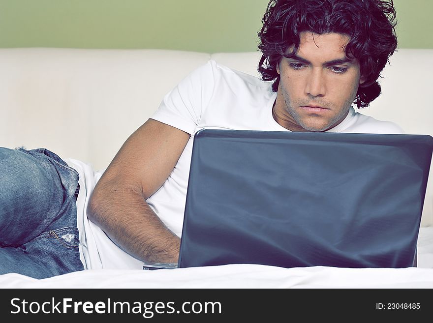 Attractive young man is working from bed with wireless laptop. Attractive young man is working from bed with wireless laptop