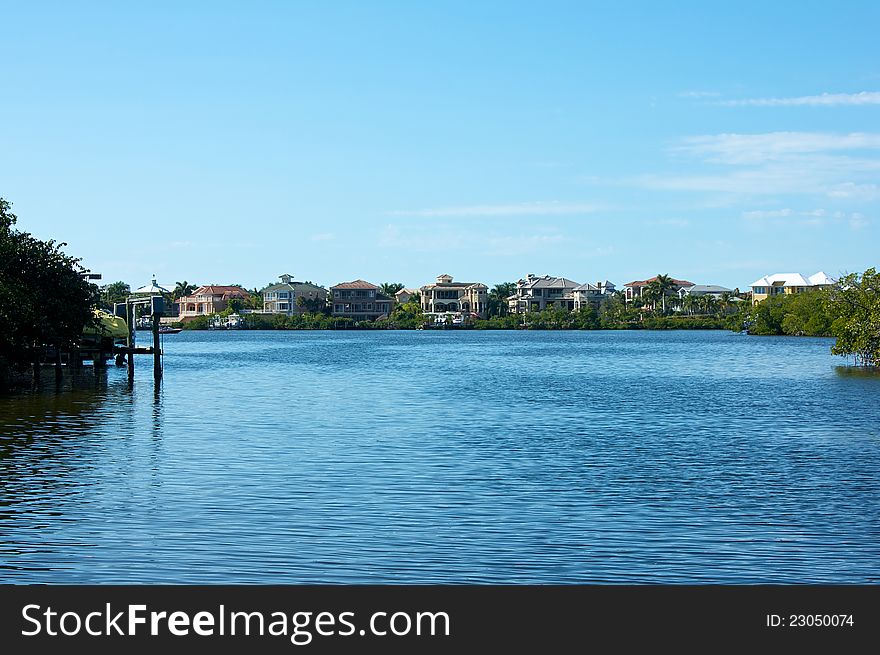Looking out across a large expanse of water towards modern Florida homes lining the riverbank on a sunny day. Looking out across a large expanse of water towards modern Florida homes lining the riverbank on a sunny day.