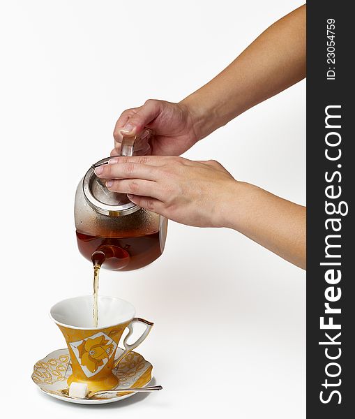 Tea being poured into glass tea cup on a white background.