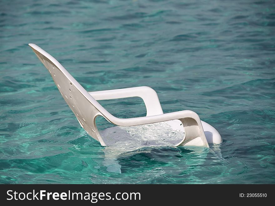 White plastic beach chair in clean blue water. White plastic beach chair in clean blue water