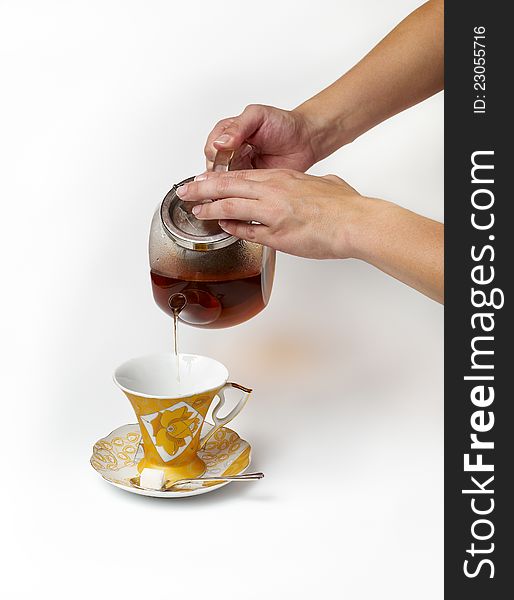 Tea being poured into glass tea cup on a white background.