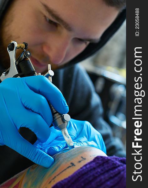 Bearded Caucasian tattooist creates a tattoo on a woman's shoulder, close up