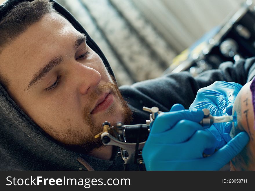 Bearded Caucasian tattooist creates a tattoo on a woman's shoulder, close up