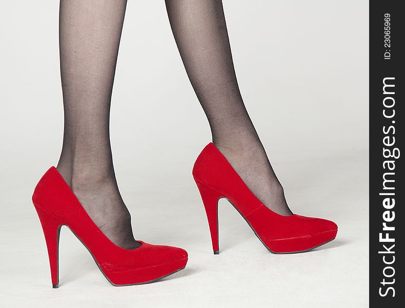 Close Up of Woman's Legs in Red Velvet High Heels and Dark Pantyhose Standing Against a White Background