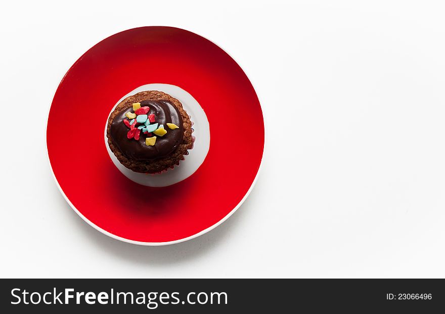 Brown delicious muffin on red plate on white background. Brown delicious muffin on red plate on white background