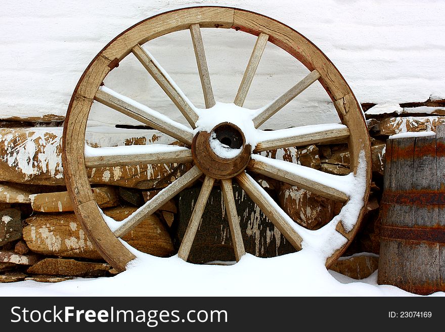 Antique wagon wheels in snow on a white brick wall with stones