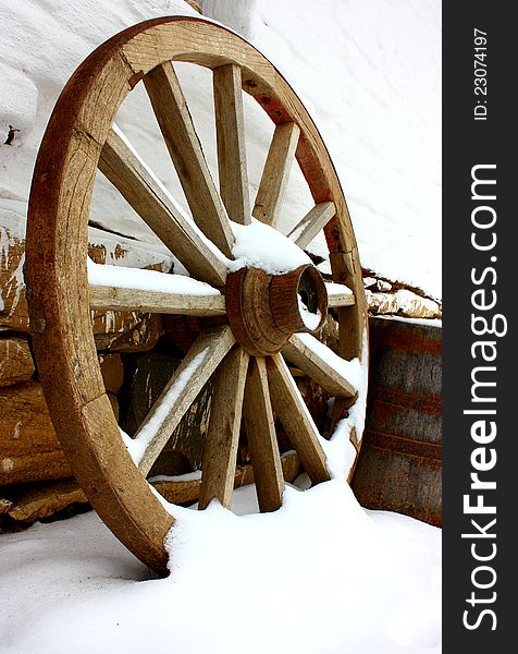 Antique wagon wheels in snow on a white brick wall with stones