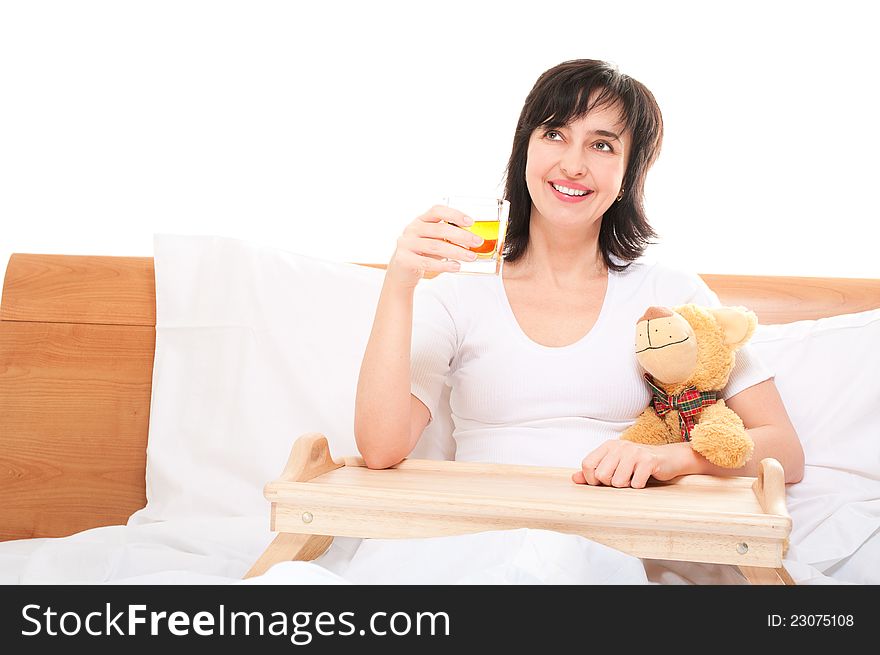 Happy dreamy woman in bed with apple juice and teddy bear isolated on white